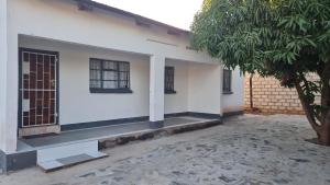 ein weißes Haus mit einem Baum davor in der Unterkunft EAGLE WEAVERS NEST in Livingstone