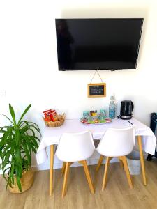 mesa blanca con sillas blancas y TV en la pared en Chambre d'hôtes de charme MERBLEUESOLEIL en Six-Fours-les-Plages