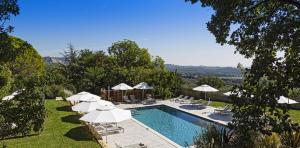 - une piscine avec des parasols blancs et des chaises à côté dans l'établissement Le Mas D'aigret, aux Baux-de-Provence