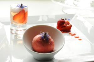 a white plate with a bowl of strawberries and a drink at La Ferme des Mares, Demeures & Châteaux in Saint-Germain-sur-Ay