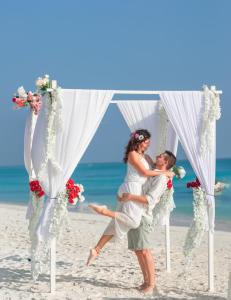 Una novia y un novio bajo un arco de boda en la playa en Alesara Guest House, en Thoddoo