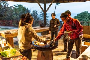 un grupo de personas preparando comida en una parrilla en アウトドアコミュニティロッジ gosen～山梨の老舗アウトドアショップ ELKから生まれたロッジ～, en Minami Alps