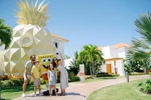 a family poses in front of the pineapple house at Nickelodeon Hotels & Resorts Punta Cana - Gourmet All Inclusive by Karisma in Punta Cana