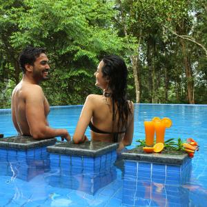 a man and a woman sitting in a swimming pool at Peter's Coffee Creek Wayanad Pool Resort and Spa in Wayanad