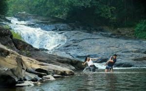 two people standing in the water near a waterfall at Peter's Coffee Creek Wayanad Pool Resort and Spa in Wayanad