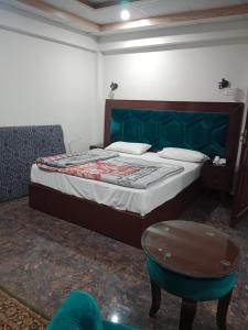 a bedroom with a bed with a green headboard and a table at AL KHALEEJ HOTEL in Murree