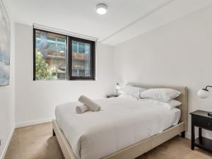 a white bedroom with a bed and a window at Light Filled Apartment by Albert Park & Lake in Melbourne