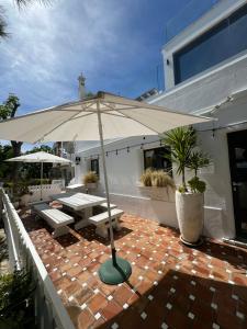 um pátio com um guarda-chuva, uma mesa e um banco em The Beach House em Vila Nova de Cacela
