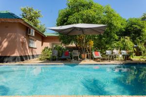 a swimming pool with an umbrella and chairs and a table at Hungwe House in Victoria Falls