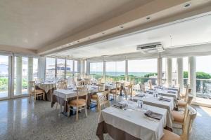 un restaurante con mesas y sillas blancas y ventanas en Hotel Villa Doimo, en Lignano Sabbiadoro
