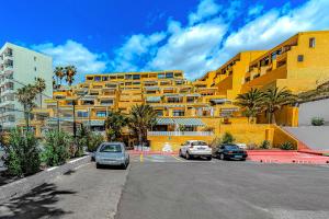 um edifício amarelo com carros estacionados num parque de estacionamento em Newly renovated studio 2 min from Playa La Arena em Puerto de Santiago