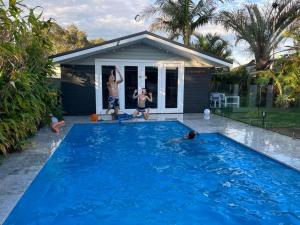 two men playing in a swimming pool in front of a house at Woy Woy Staycation - Heated Pool & Hot Tub & BBQ & Pizza Oven & Arcade Game & Pool Table in Woy Woy