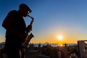 mężczyzna grający na saksofonie na plaży o zachodzie słońca w obiekcie Riva di Ugento Beach Camping Resort w mieście Ugento