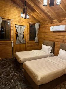 two beds in a room with wooden walls and windows at KRZ Cottages أكواخ الكرز in Al Shafa