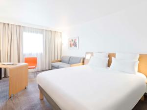 a hotel room with a large white bed and a chair at Novotel Saint-Quentin en Yvelines in Magny-les-Hameaux