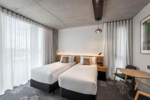 a hotel room with two beds and a desk and a table at Vibe Hotel Adelaide in Adelaide