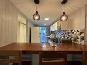 uma cozinha com uma mesa de madeira e luzes pendentes em Apto com VISTA ESPETACULAR a BEIRA MAR no Pecado - Wi Fi 200 mb - 2 Quartos - Garagem - TV Smart - Piscina - Sauna - Ar condicionado - Portaria 24h - Churrasqueira - Cozinha equipada em Macaé
