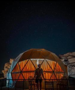 Un uomo che di notte sta davanti a una yurta di RUM EiLEEN LUXURY CAMP a Wadi Rum