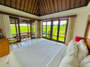 a bedroom with a large bed in a room with windows at Umah Teresna in Ubud