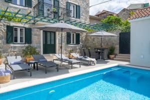 a pool with chairs and umbrellas next to a house at Villa Filipetti in Makarska center, 4 en-suite bedrooms charming stone house, heated private pool, 600m from beach in Makarska +42 photos
