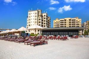 una fila di sedie e ombrelloni su una spiaggia con edifici di Marina Views Al Hamra Village a Ras al Khaimah