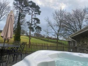 a hot tub with a table and an umbrella at Bwthyn Derrick in Tal-gareg