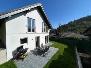 a white house with a patio and a grill at Wellness-Ferienhaus mit Dampfbad & Sauna am Nürburgring in Leimbach