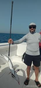 Un uomo in piedi su una barca con un palo di Dubai fishing trip 5 hours a Dubai