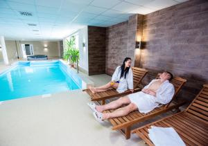 duas pessoas sentadas em cadeiras ao lado de uma piscina em Hotel Median Hajdúnánás em Hajdúnánás