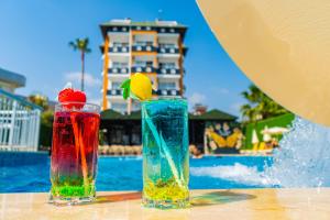 dois copos coloridos sentados numa mesa ao lado de uma piscina em DE MARE FAMILY Hotel em Konaklı