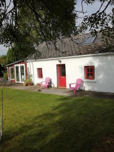 uma casa branca com cadeiras cor-de-rosa e uma porta vermelha em Quaint secluded Cottage close to beautiful Kinvara em Gort
