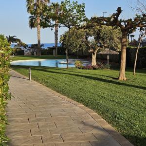 un chemin en briques dans un parc planté d'arbres et d'herbe dans l'établissement Apartamento con piscina en una preciosa playa, à Alcossebre