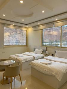 Cette chambre comprend 3 lits, une table et 2 fenêtres. dans l'établissement Viola desert, à Al-Ula