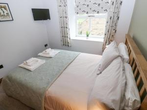 a bedroom with a bed with white sheets and a window at Bumble Cottage in Holmfirth