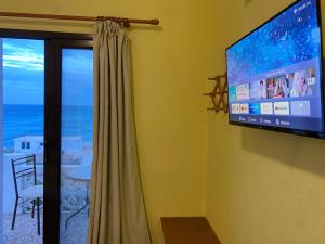 Elle comprend une télévision à écran plat suspendue sur un mur à côté d'une fenêtre. dans l'établissement Studio Apartments, à Diafani