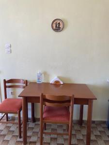 une table en bois avec deux chaises et une horloge sur le mur dans l'établissement Studio Apartments, à Diafani