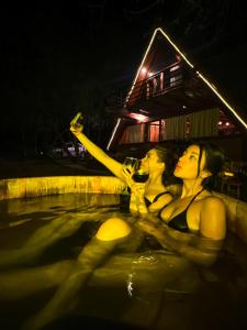 two women sitting in a swimming pool drinking wine at Chalet privado en el bosque con Jacuzzi de Madera Huasca Retreats in Huasca de Ocampo