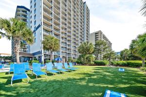 a row of blue chairs on a lawn in front of a building at Beach Colony Resort in Myrtle Beach