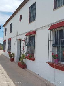 a white building with red windows and plants on it at Casa El Azahin in Cazalla de la Sierra