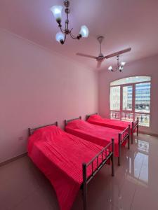 2 Betten in einem Zimmer mit roter Bettwäsche und einem Fenster in der Unterkunft Blue Umbrella in Muscat