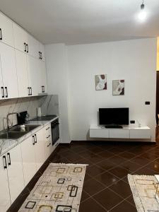 kuchnia z białymi szafkami, zlewem i telewizorem w obiekcie Iri Apartment w Durrës