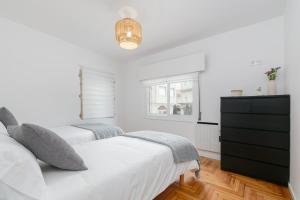 a white bedroom with two beds and a dresser at Ohana Home in Porriño