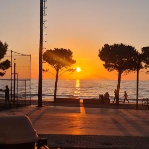 um pôr do sol sobre o oceano com pessoas caminhando na praia em Sunset House em Vlorë