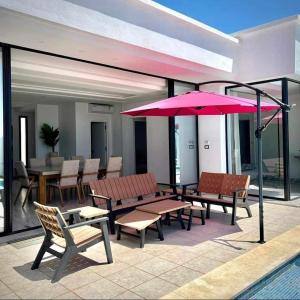 une terrasse avec des bancs et un parasol rose dans l'établissement villa Casa Luxe djerba, à Mezraya