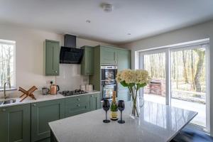 a kitchen with green cabinets and a table with wine glasses at Padley; woodland lodge with hot tub for 2-4 in the Staffordshire Moorlands in Oakamoor