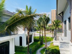 - un balcon offrant une vue sur un bâtiment avec des palmiers dans l'établissement V3E02 Dahlia villa - khu nghỉ dưỡng Sonasea Vân Đồn, à Cái Rồng
