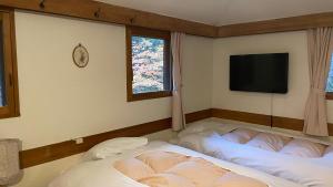 2 camas en una habitación con TV en la pared en 乗鞍高原の宿テンガロンハットB&BTengallonhat, en Matsumoto
