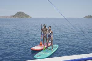 two girls are standing on a paddle board in the water at Leticia Liveaboard in Labuan Bajo