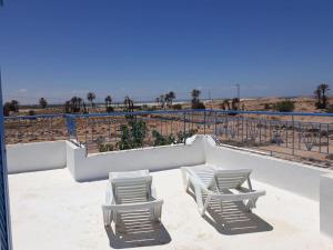 zwei weiße Stühle auf einem Balkon mit Strand in der Unterkunft Villa Yahia Djerba in Bou Menjel