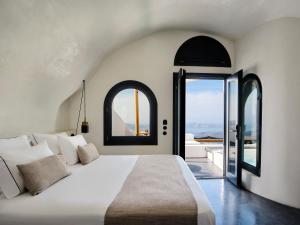 una camera da letto con un grande letto bianco con due finestre di Stella Rocca A Mare a Imerovigli